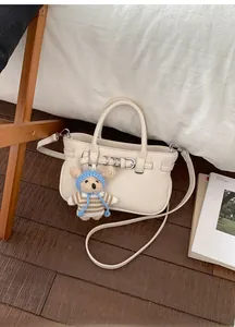 Detail der cremefarbenen Ledertasche mit Silberschnalle und süßem Bärenanhänger