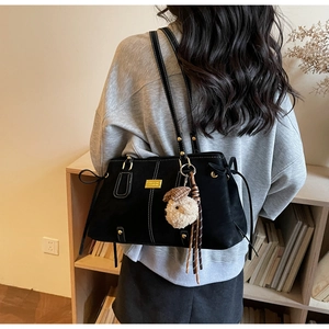Detail of a black suede tote bag with white contrast stitching and a plush puppy charm