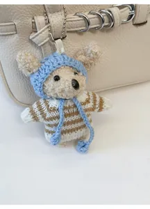 Detail eines süßen Plüschtier-Anhängers mit Strickmütze an einer beigen Ledertasche