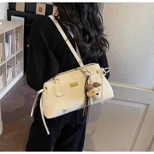 Detail of a creamy white shoulder bag with a cute plush bear charm and side bow decoration
