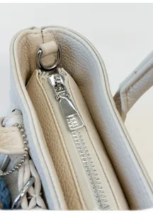 Detail eines silbernen Metallreißverschlusses an einer beigen quadratischen Handtasche
