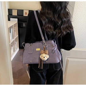 Detail of purple faux leather tote bag with teddy bear charm and gold logo plate