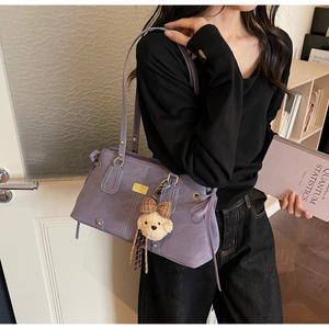 Detail of purple suede shoulder bag with gold hardware and teddy bear charm