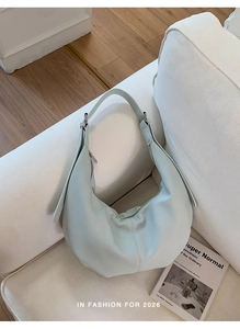 Nahaufnahme einer mintgrünen Hobo-Tasche aus Leder auf einem Sofa neben einem Buch