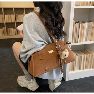 Detail of vintage brown suede tote bag with a cute plush bear charm and metallic plate