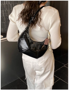 Detail of black crescent shoulder bag with silk scarf and chocolate charm on model