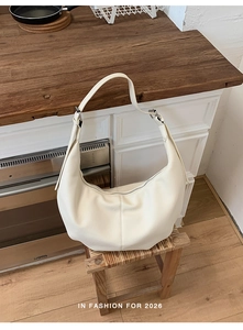 Detailansicht einer cremefarbenen Hobo-Tasche auf einem Holzhocker in moderner Umgebung