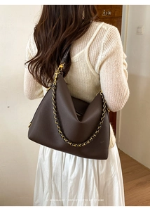 Detail of soft brown pebble leather shoulder bag with golden chain accent on a model