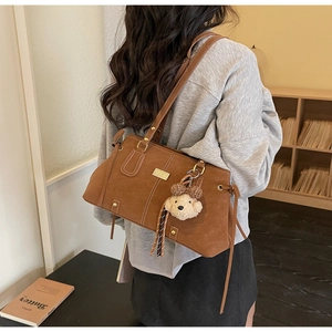 Brown suede tote bag detail with gold hardware, plush bear charm and tassel accents