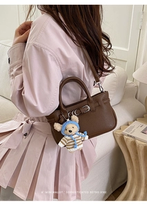 Detail einer braunen Handtasche aus Leder mit Bärenanhänger und Retro-Schnalle