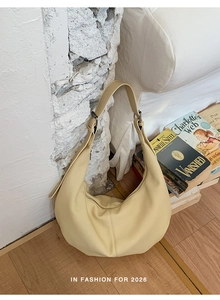 Detail einer cremefarbenen Halbmond-Tasche mit weicher Ledertextur und verstellbarem Gurt