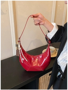 Detail of red patent leather crescent bag with chocolate pendant and strap decor