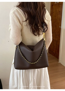 Close-up of brown pebbled leather tote bag featuring gold hardware and woven chain detail