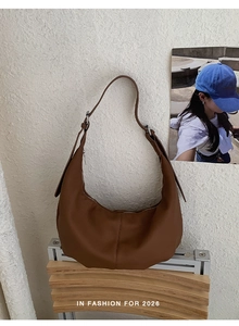 Braune Hobo-Schultertasche mit Narbenleder-Textur auf Holzständer bei natürlichem Licht