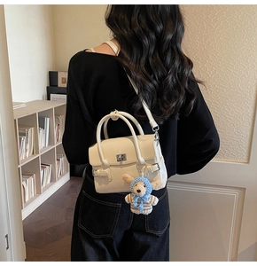 Detail of cream white leather shoulder bag with silver turn-lock and plush puppy charm