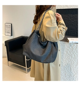 Detail view of black denim hobo bag with chain strap styled with a trench coat
