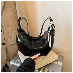 Detail of black glossy hobo bag with artistic chain and chocolate-shaped charm