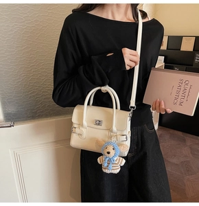 Detail of cream white leather handbag with silver lock and a cute plush dog charm