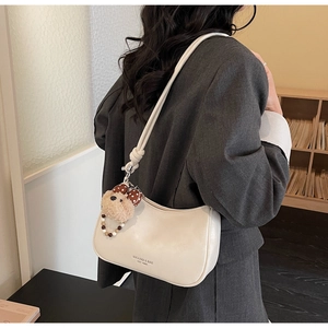 Chic beige shoulder bag with teddy bear charm shown on model in cozy indoor setting