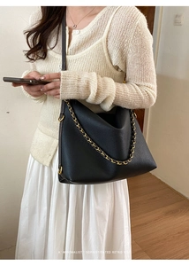 Detailed view of a black pebble leather hobo bag featuring a gold chain and wide strap
