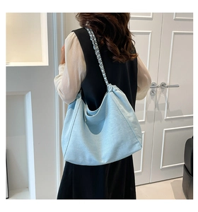 Detail of light blue denim tote bag showing metal chain strap and woven texture