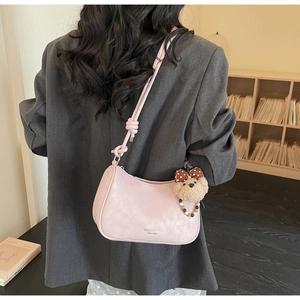 Pink underarm bag with knot strap detail and cute plush bear charm on a female model