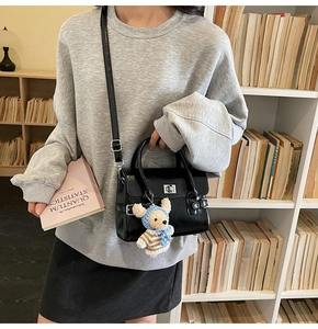 Detail of a black glossy handbag with silver rotary buckle and a cute bear charm