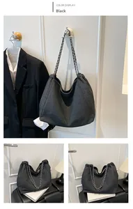 Detail of black textured denim tote bag featuring dual metal chain straps and drawstring top