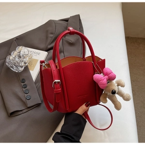 Detail of red pebbled leather tote featuring a plush puppy charm and pink ribbon bow