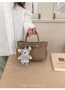 Detail der khakifarbenen Ledertasche mit Metallschnalle und süßem Bären-Anhänger