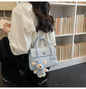 Detail of light blue patent leather handbag with silver clasp and cute teddy bear charm