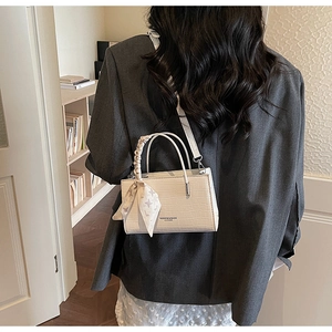 Detailed view of white crocodile pattern handbag with printed silk scarf on handle