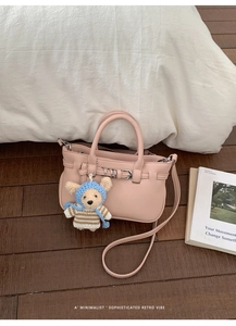 Detail der rosa Handtasche mit Lederstruktur und Bären-Anhänger auf Holzboden