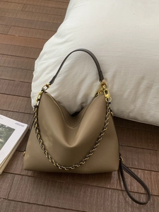 Minimalist khaki leather tote bag with wide strap and gold chain on wooden floor