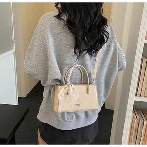 Detail of beige faux crocodile leather bag with silk scarf on handle and shoulder strap