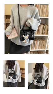 Detail of black crossbody bag with silver clasp and cute plush bear charm on strap