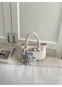 Schicke cremefarbene Lederhandtasche mit Silberringen und süßem Teddybär-Anhänger im Detail