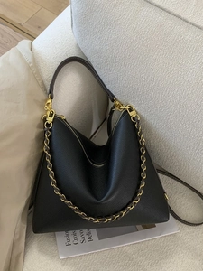 Chic black lychee leather hobo tote bag with gold chain strap on sofa background