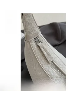 Close-up of metal zipper closure on white pebble leather shoulder bag with neat stitching