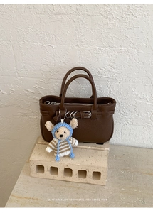 Detail der dunkelbraunen Lederhandtasche mit Metallringen und süßem Bären-Anhänger