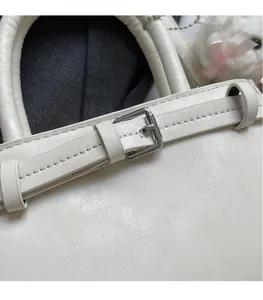 Detail of white faux leather tote bag with silver metal buckle and decorative strap