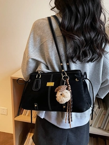 Black leather tote bag with white stitching and plush sheep charm in casual setting