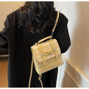 Detail of yellow checkered crossbody bag with bow accent worn on black long coat