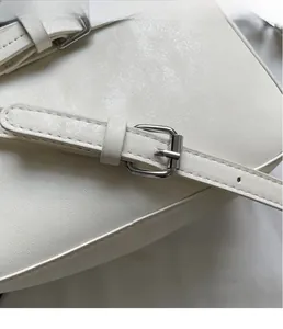 Detailed close-up of white leather handbag with silver metal buckle and neat stitching