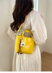 Dettaglio di una borsa a secchiello giallo acceso con ciondolo a fiori su abito bianco