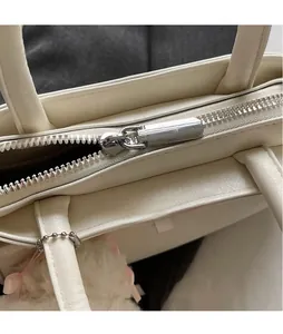 Detail of silver metallic zipper and smooth off-white leather texture on handbag