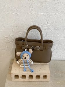 Braune Handtasche aus Leder mit Doppelgriff und süßem Teddybär-Anhänger auf Steinbasis