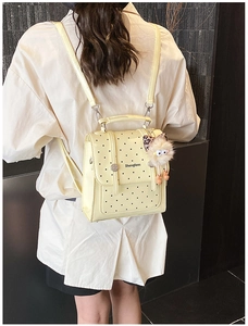 Close-up of a yellow mini backpack with black polka dots and a plush monster charm