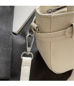 Close-up of silver metal hook and refined lychee grain leather strap on a cream bag