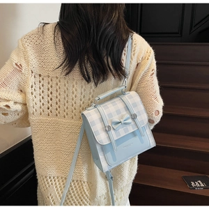 Blue and white checkered leather shoulder bag with bow detail worn on stairs